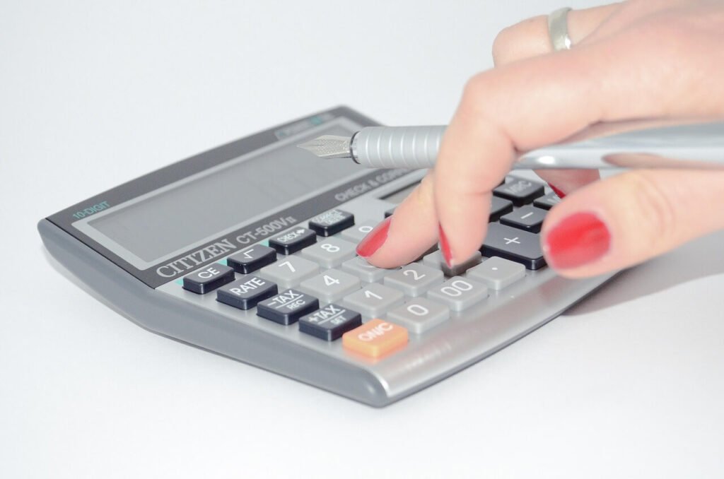 Hand with red nail polish pressing calculator buttons with a pen, symbolizing calculating credit scores and financial analysis.