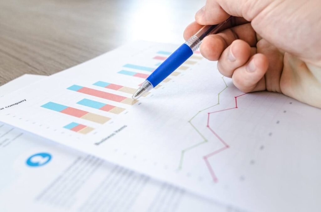 Hand holding a pen pointing at colorful bar and line charts on paper, representing financial data trends.
