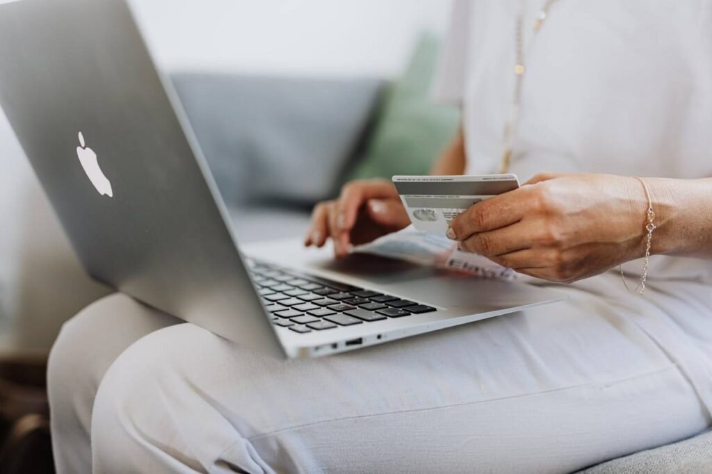 Person holding a credit card while using an Apple MacBook.