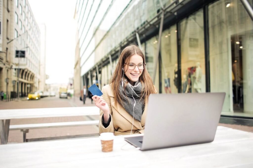Smiling woman sitting outdoors with a laptop and holding a bank card.